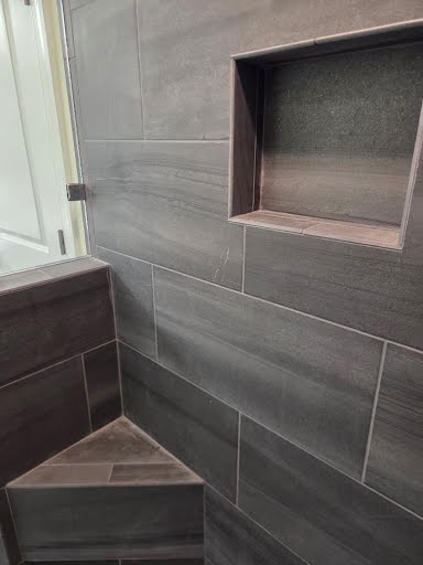 Large-format gray tile shower with a recessed shampoo niche and tiled corner bench seat