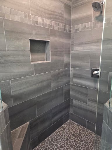 Shower interior with gray plank tile, mosaic accent band, recessed niche, and pebble tile floor